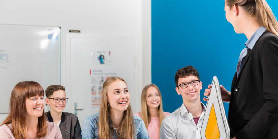 Fahrschülerinnen und Fahrschüler im Theorieunterricht mit Fahrlehrerin und Verkehrszeichen